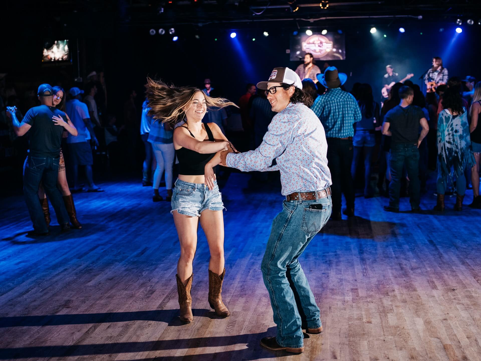 Couples dancing on the hardwood floor with a band on stage under blue lights